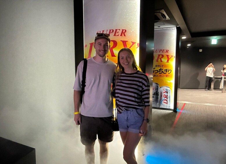 Two people standing in front of a wall with a large advertisement for a beverage. 3
