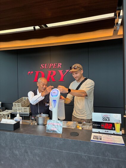 Two people at a bar counter with a sign reading 'SUPER DRY'. 2