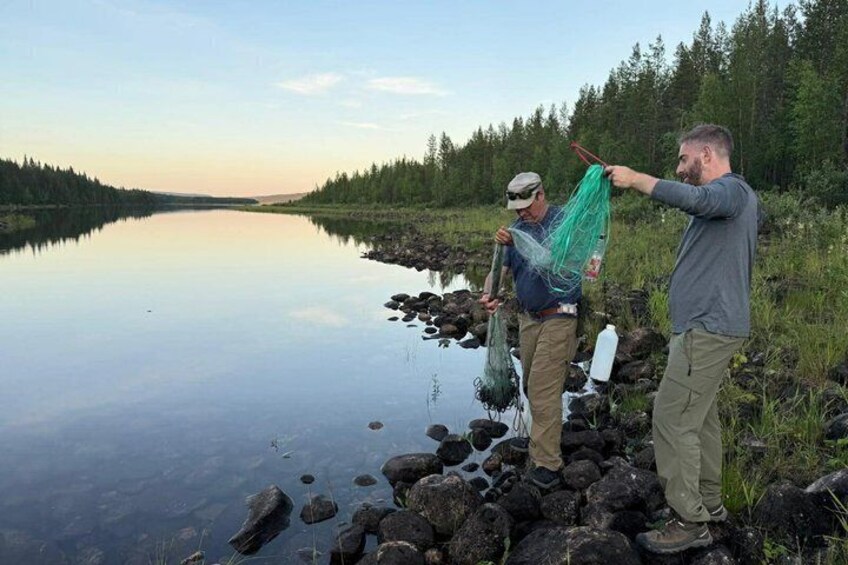 Two people fishing by a calm lake surrounded by forest. 1