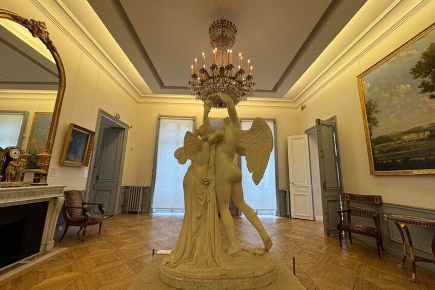 Une vaste pièce ornée d’un grand lustre, d’une statue d’ange et d’un tableau accroché au mur. 3