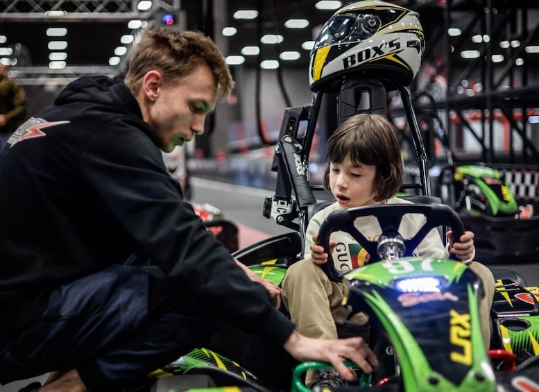 A person in a black hoodie sitting next to a child in a go-kart, both holding steering wheels. 3