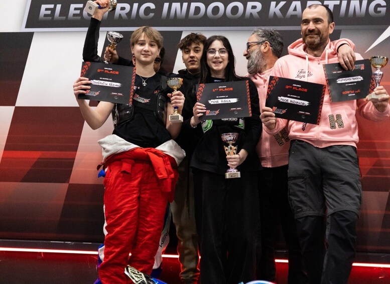A group of people holding trophies at an indoor karting event. 2