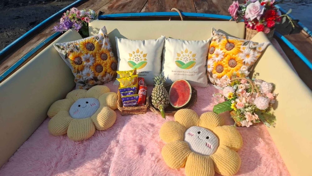 A boat interior with floral pillows, a knitted flower, a basket with snacks, and a watermelon. 5