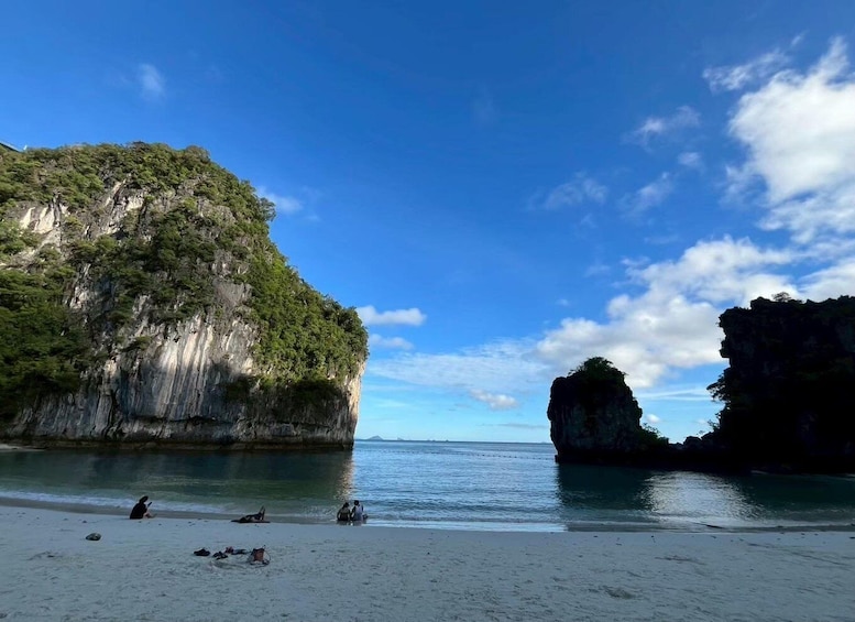 A beach with clear water, a large cliff, and a smaller rock formation. 4