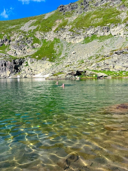 A clear mountain lake with rocky shores and two people swimming. 2