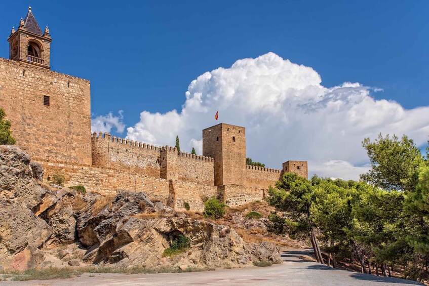 A historic stone fortress with battlements, a watchtower, and a flag atop a tower. 1