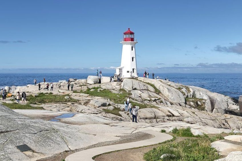 A lighthouse on a rocky outcrop with people walking around. 1
