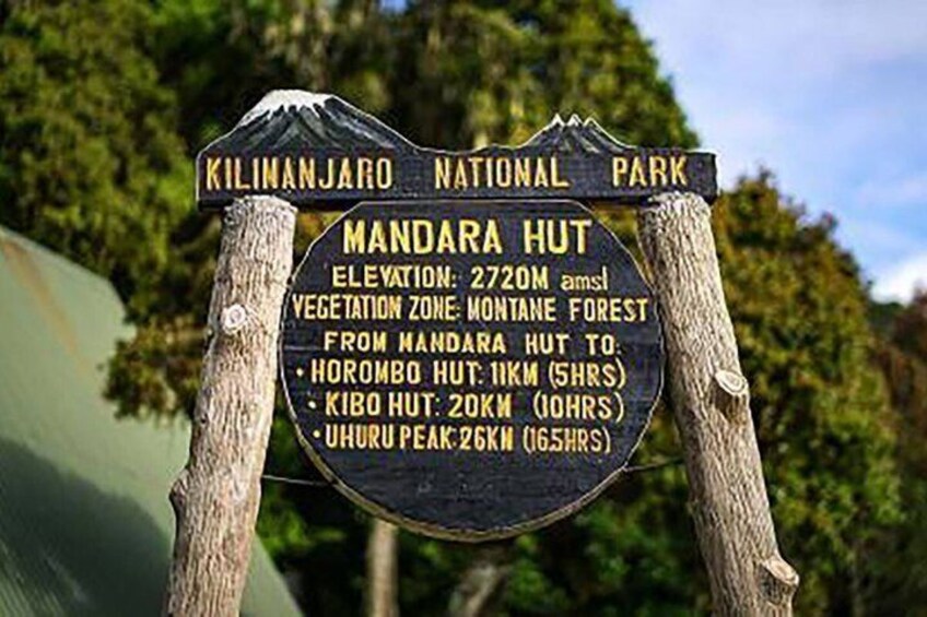 A signpost with information about Kilimanjaro National Park, Mandara Hut, and hiking distances to nearby huts and peaks. 5