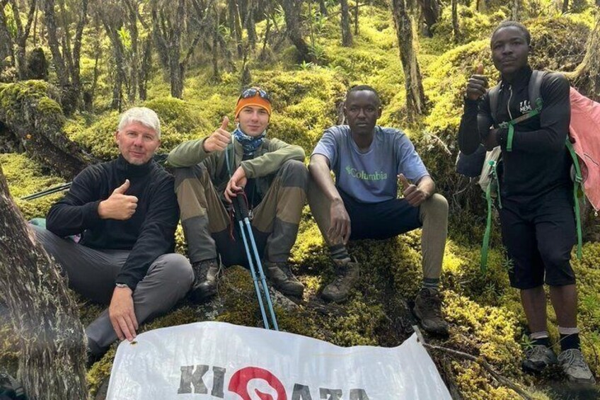 Four people in a forested area with a white bag labeled 'KIA' on the ground. 3