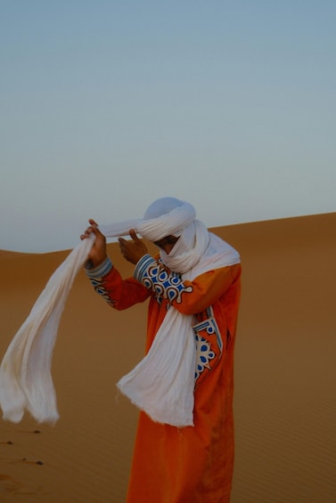 A person in traditional attire adjusting a white garment in a desert landscape. 2