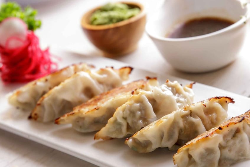 A plate of pan-fried dumplings with a dipping sauce and a side of pickled vegetables. 5
