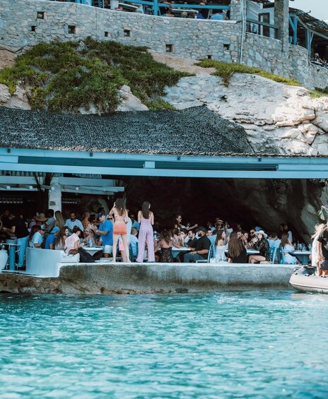 A stone building with a thatched roof, a crowd of people, and a body of water. 1