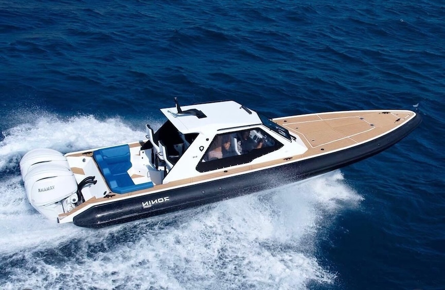 A speedboat with a white and black hull, blue seating, and a cabin, moving through the water. 4