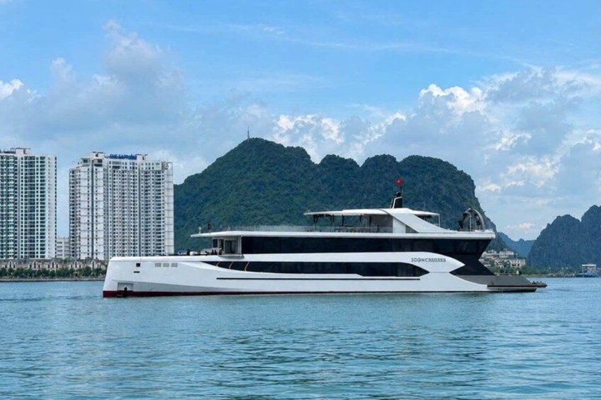 A large, multi-deck yacht on calm waters with a mountainous coastline in the background. 1