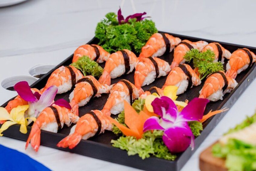 A tray of sushi rolls with seaweed, garnished with flowers and green leaves. 3