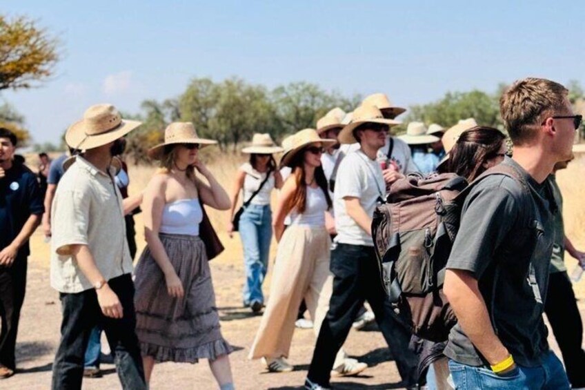 Un grupo de personas caminando al aire libre, algunas con sombreros y cargando mochilas. 2