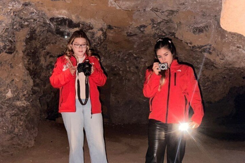 Dos personas con chaquetas rojas dentro de una cueva, iluminadas con una linterna. 3
