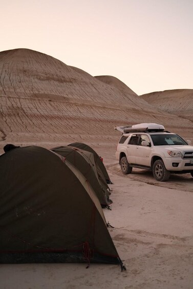A white SUV parked in a desert with tents set up nearby. 3