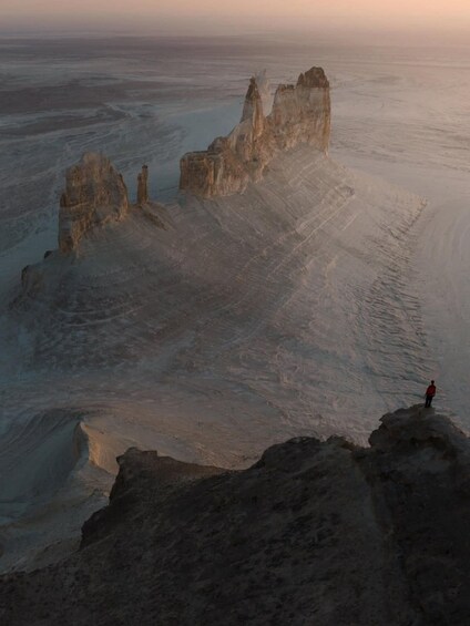 A person standing on a rock formation in a vast desert landscape. 3