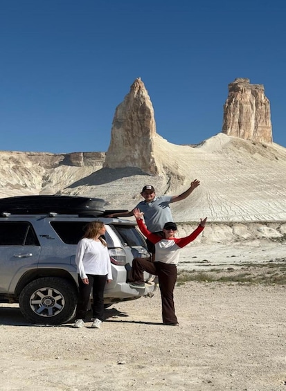 A group of people standing in front of a rocky landscape with a prominent rock formation in the background. 1