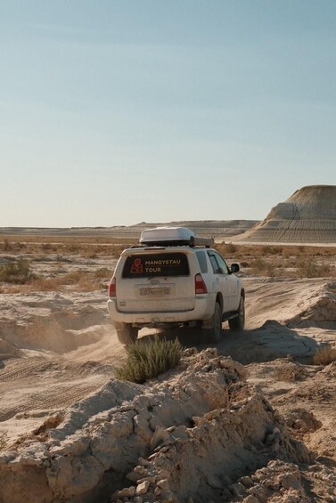 A white off-road vehicle with a roof rack and a sign reading 'MANGYSTAU TOUR' on a desert landscape. 4