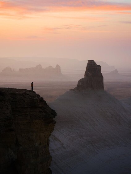 A person standing on a cliff overlooking a vast desert landscape with rock formations. 2