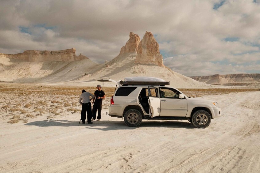 A white SUV parked on a desert road with two people standing beside it. 2