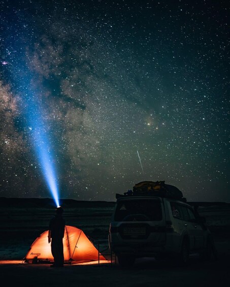 A person standing next to a tent under a starry sky with a vehicle in the background. 5