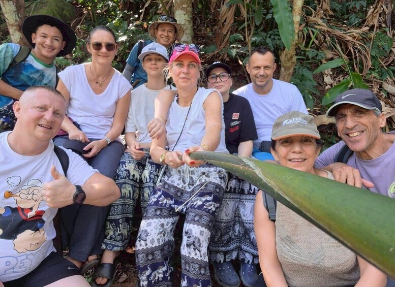A group of people outdoors, some holding a large leaf, surrounded by dense foliage. 1
