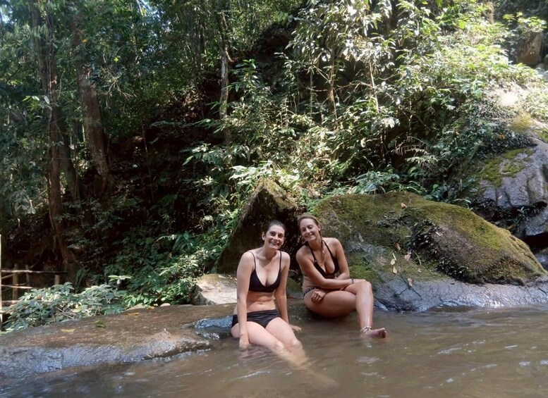 Two people sitting on a rock by a stream in a forested area. 3