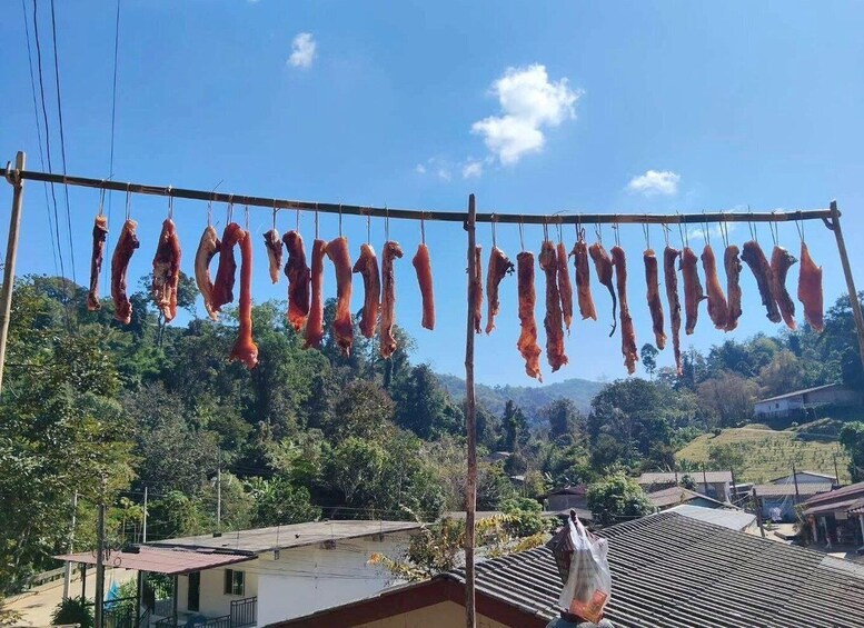 Hanging meat drying on a line in a rural setting with houses and hills in the background. 5