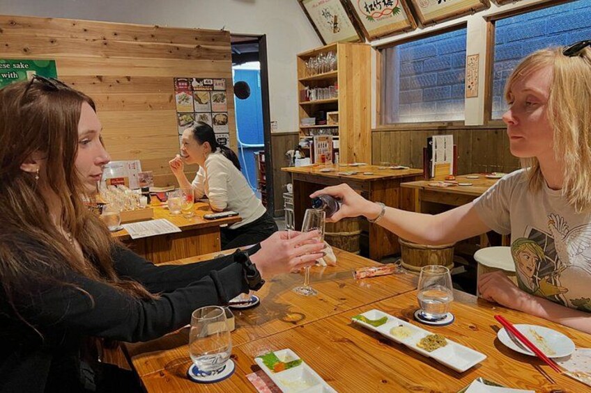 A wooden interior with tables, people dining, and a menu board. 2