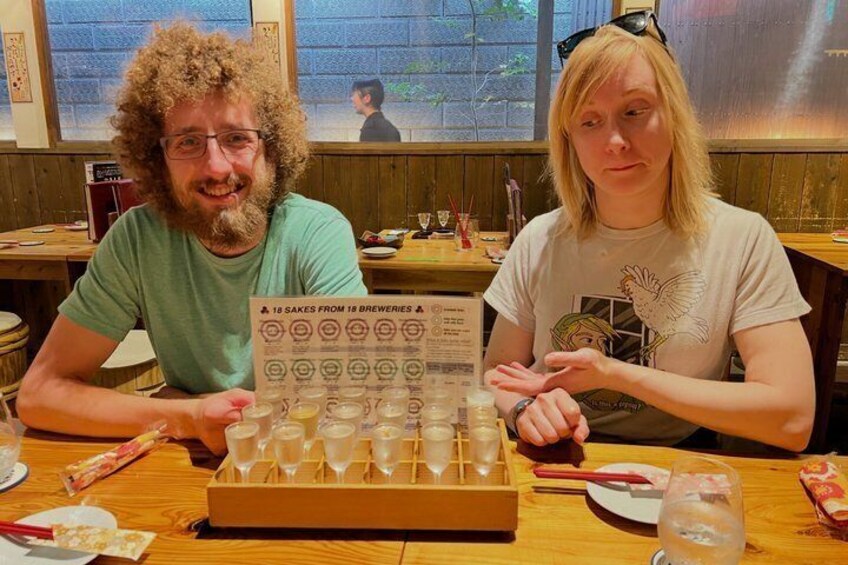 Two people at a table with a tray of shot glasses and a menu. 5