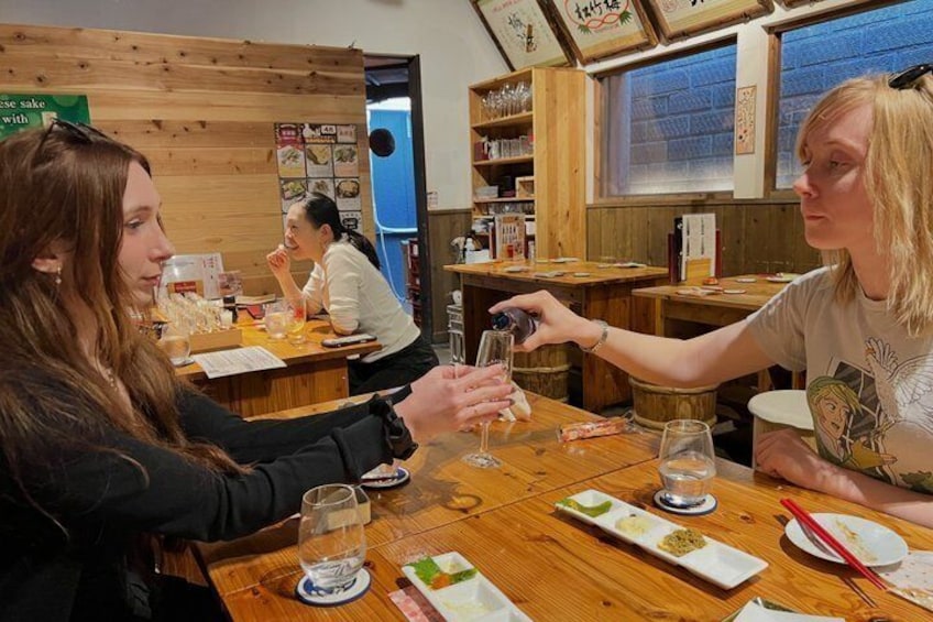 Two people toasting at a wooden table in a restaurant with other patrons in the background. 2