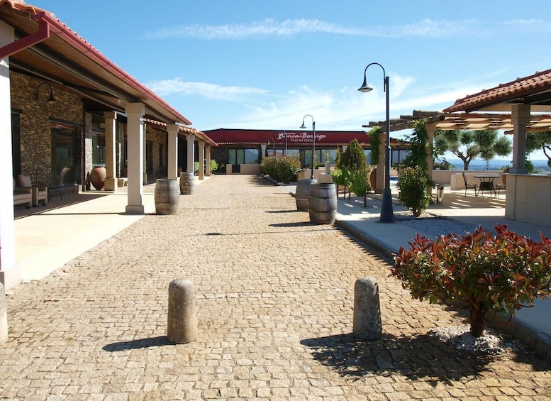 A cobblestone pathway leading to a building with a red roof, stone pillars, and outdoor seating. 3