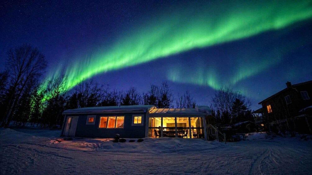 A house with a lit interior, snow-covered ground, and the aurora borealis in the sky. 5