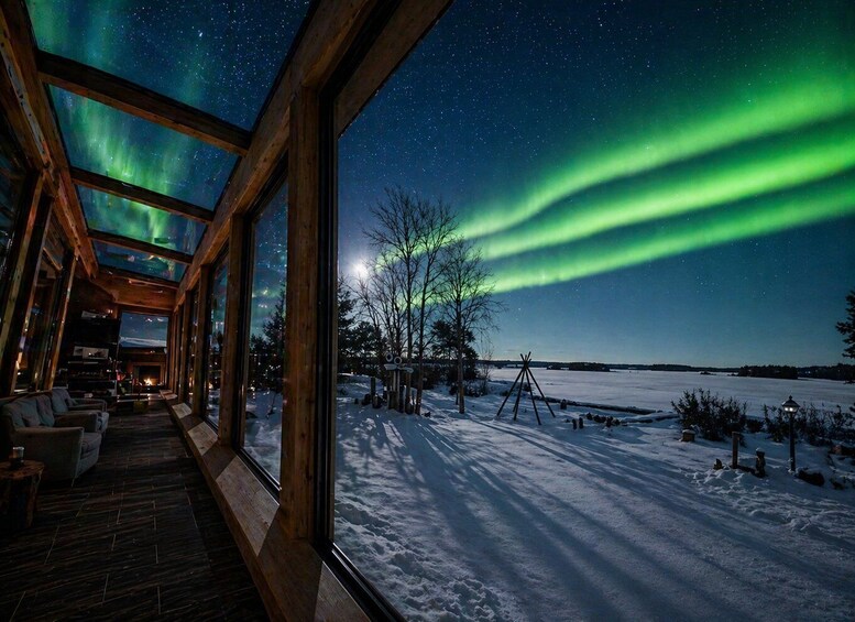 A wooden cabin with large windows overlooking a snowy landscape and the Northern Lights. 3