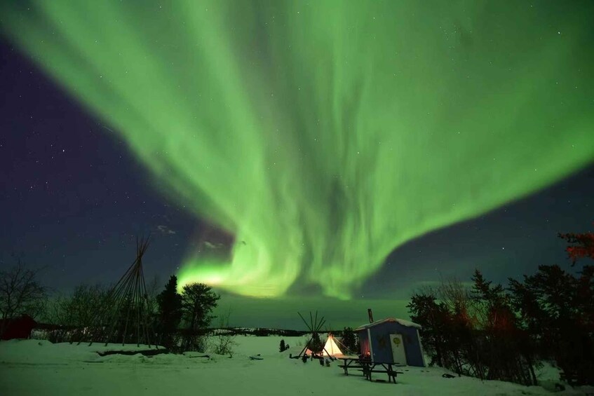 A snowy landscape with a teepee and a small cabin under a vibrant northern lights display. 4