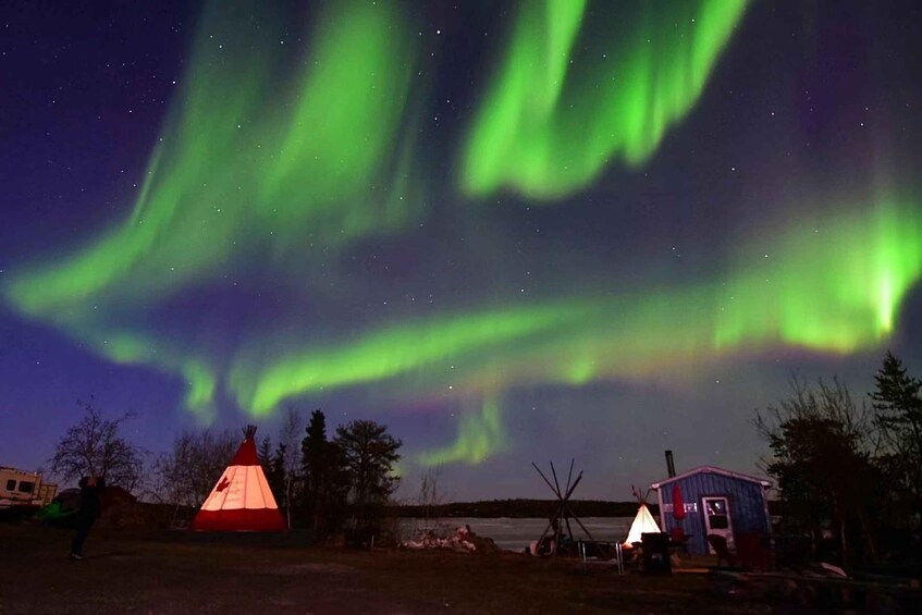 The Northern Lights over a campsite with tents and a small cabin. 1