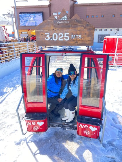 A red cabin with '3.025 MTS' and 'Valle Nevado' on a wooden sign, surrounded by snow. 3