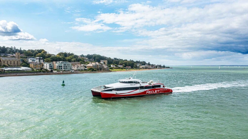 A Red Jet ferry moving across a calm body of water with a coastal town and a bridge in the background. 5