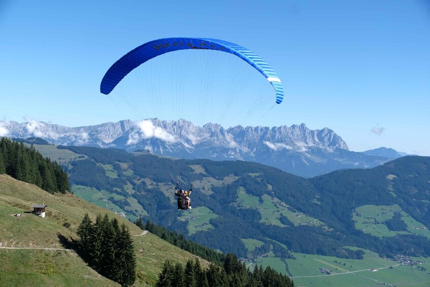 A paraglider with a blue canopy flying over a mountainous landscape. 5