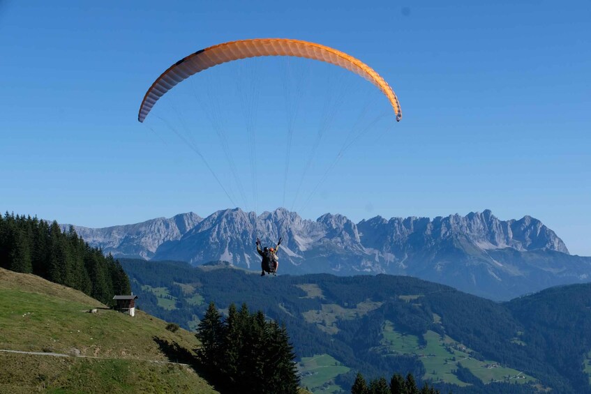 A paraglider in mid-flight over a mountainous landscape with a clear sky. 3