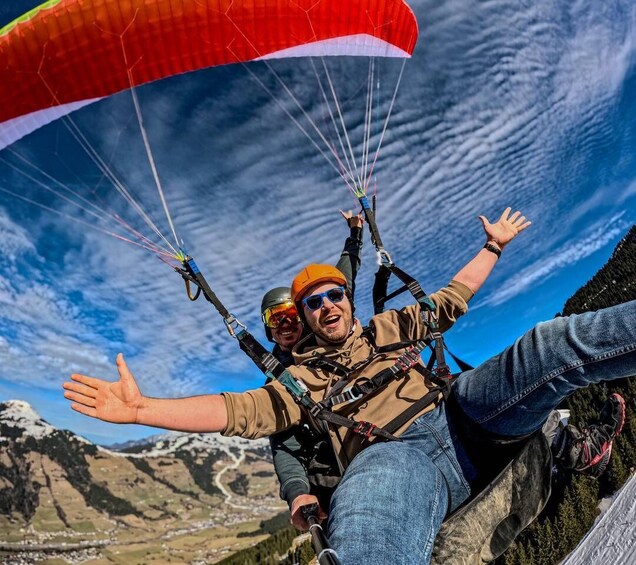 Two people paragliding with a mountainous landscape in the background. 2