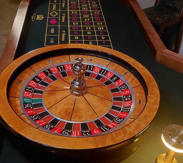 A roulette wheel with a ball in the center, a betting table with numbers, and a chair in the background. 1