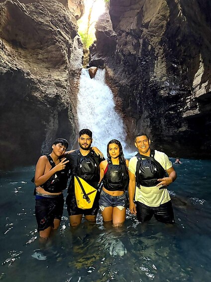 A group of people standing in a water-filled cave with a waterfall in the background. 1