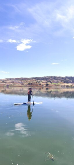 A person paddleboarding on a calm lake with a hilly landscape in the background. 1