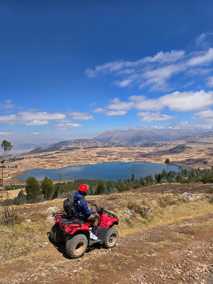 A person on a red ATV overlooking a lake and mountains. 2