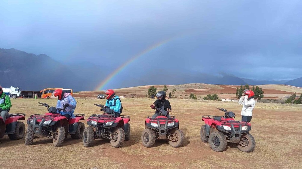 Four people on quad bikes in a field with a rainbow and mountains in the background. 3