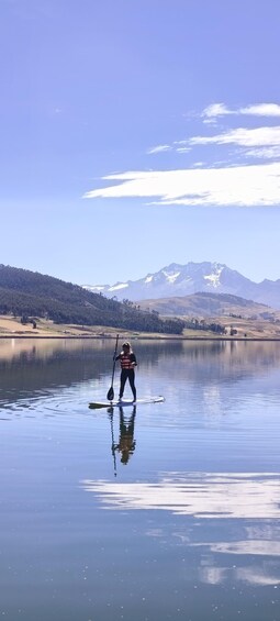 A person paddleboarding on a calm lake with mountains in the background. 2